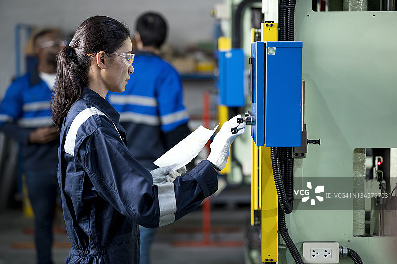 亚洲女工在生产线上操作自动化小型压力机，生产汽车零部件图片素材