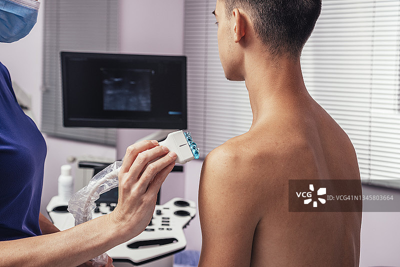 医生在年轻成年患者的肩膀上使用超声扫描仪图片素材