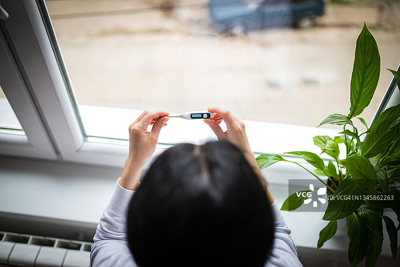 年轻女人在看温度计，她发烧了图片素材