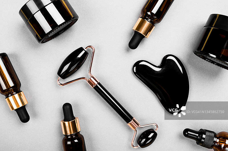 面部按摩器、黑玛瑙面部滚轮、面霜罐和面部精华瓶、抗衰老刮痧按摩、护肤和化妆品概念图片素材