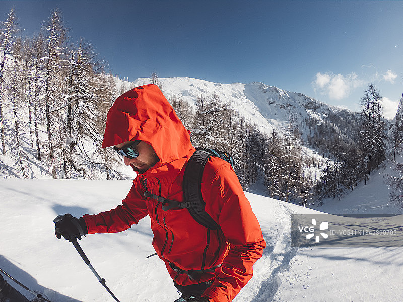 在一个阳光明媚的冬日，穿着红色夹克的登山运动员在雪地上行走图片素材