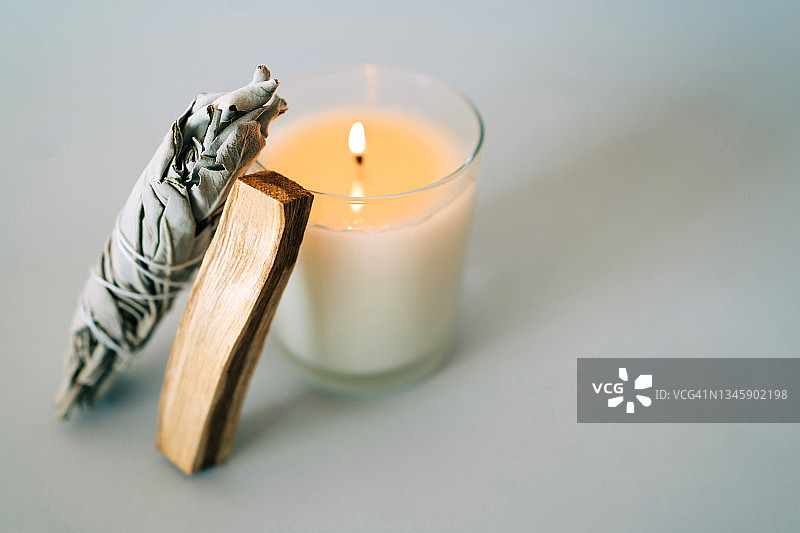 灰色背景上的圣木条、白鼠尾草和燃烧的蜡烛，用于芳香疗法和仪式，有文案空间。图片素材