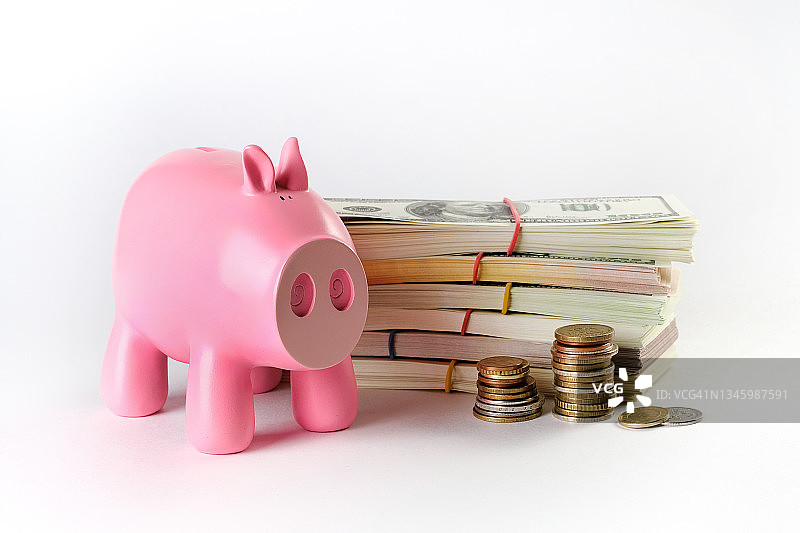 纸币，白色背景或桌子上成捆的美元。附近有一个粉红猪形状的储蓄罐。来自不同国家的货币和硬币。商业和金融、保险、投资和资金积累的概念图片素材