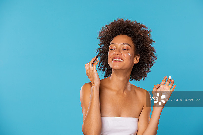 深色皮肤美女：年轻漂亮的非洲裔美国女性在蓝色背景下涂抹护肤霜图片素材