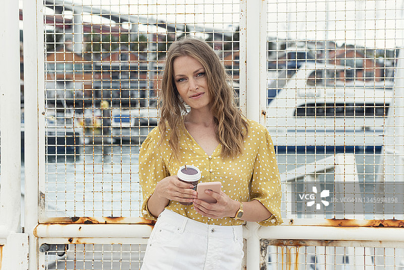 手持咖啡杯和手机的美丽女人图片素材