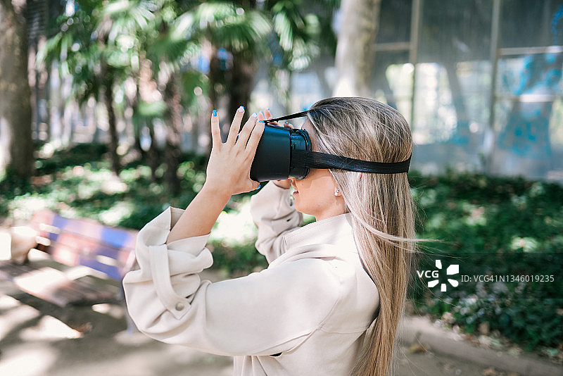 在公园体验虚拟现实的年轻女士侧面照图片素材