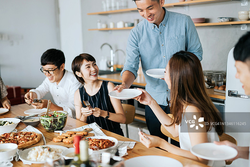 一群快乐的年轻朋友一起享受，聊天，在聚会上玩乐。男人递给朋友们盘子，准备享用美食和饮料图片素材