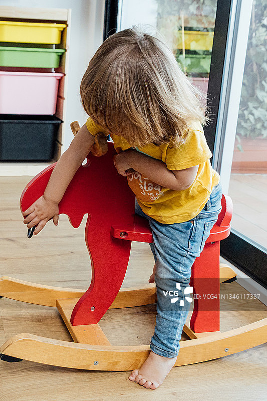 小女孩在客厅里骑木马玩具图片素材