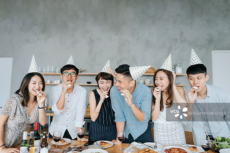 一群年轻快乐的朋友戴着派对帽，玩着派对吹气玩具，一起庆祝玩乐图片素材
