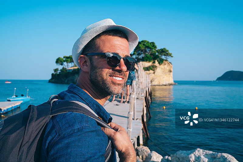 戴着太阳镜和背包的白人男游客在希腊海边欣赏风景图片素材