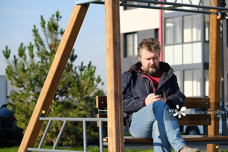 中年男人坐在长椅上使用手机图片素材