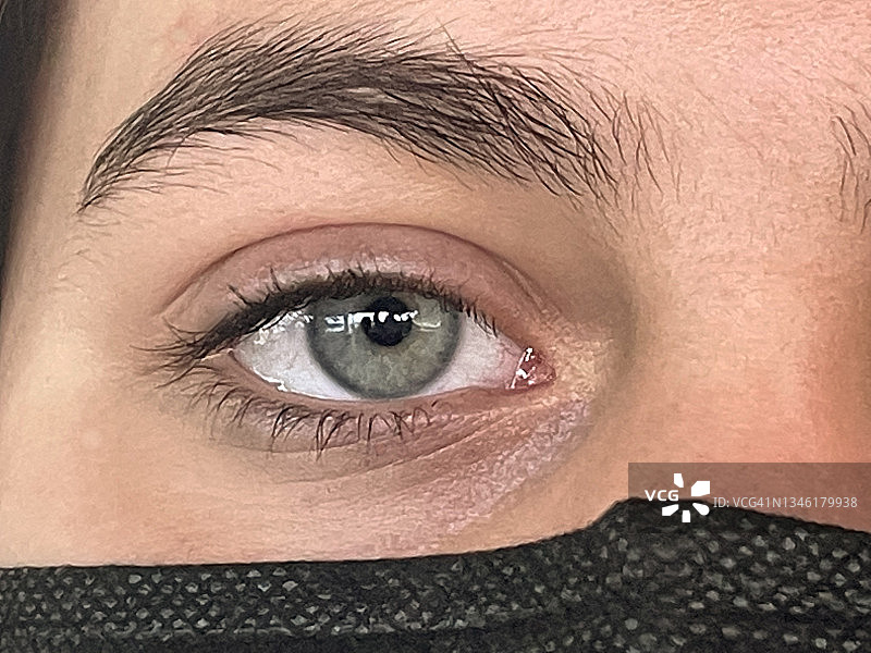 特写：戴着黑色口罩的青少年的蓝色眼睛直视镜头图片素材