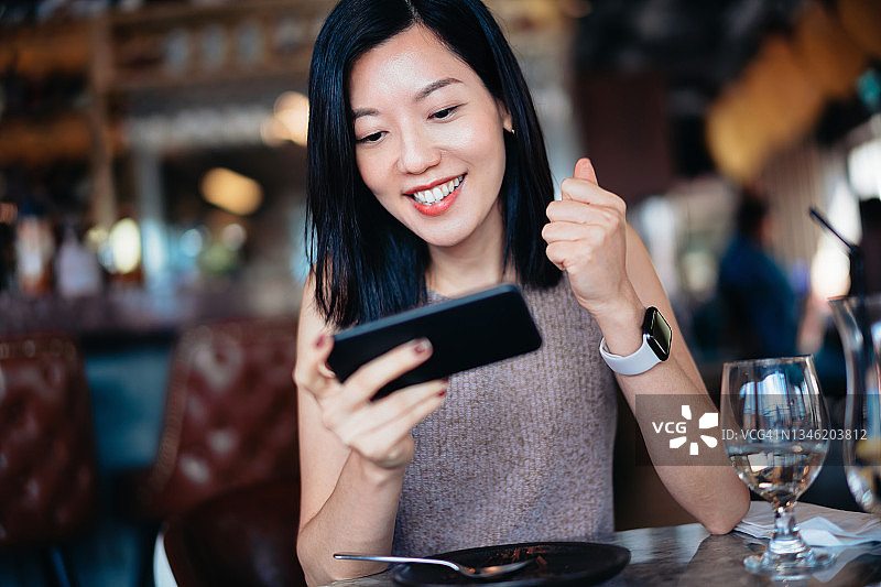 年轻的亚洲女人看着智能手机欢呼雀跃，庆祝收到好消息图片素材