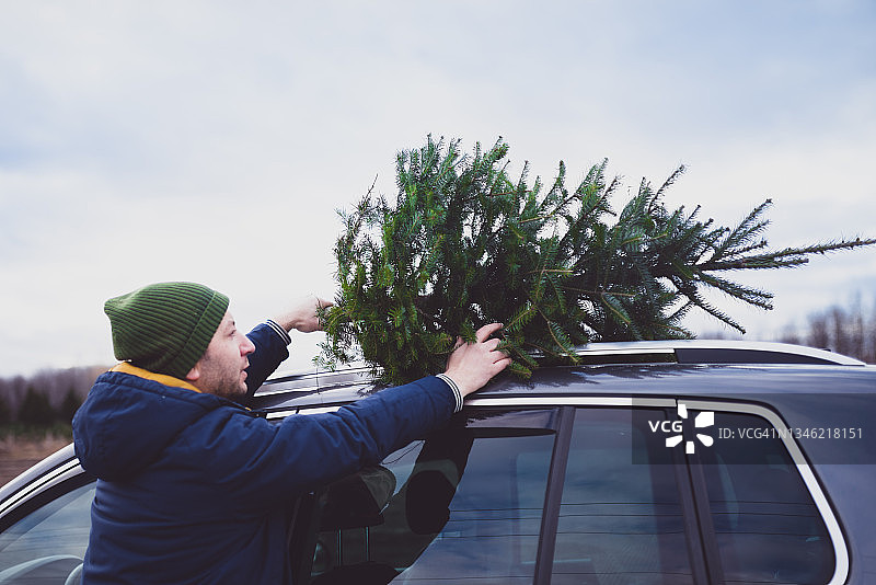 男人把圣诞树放在汽车顶部图片素材