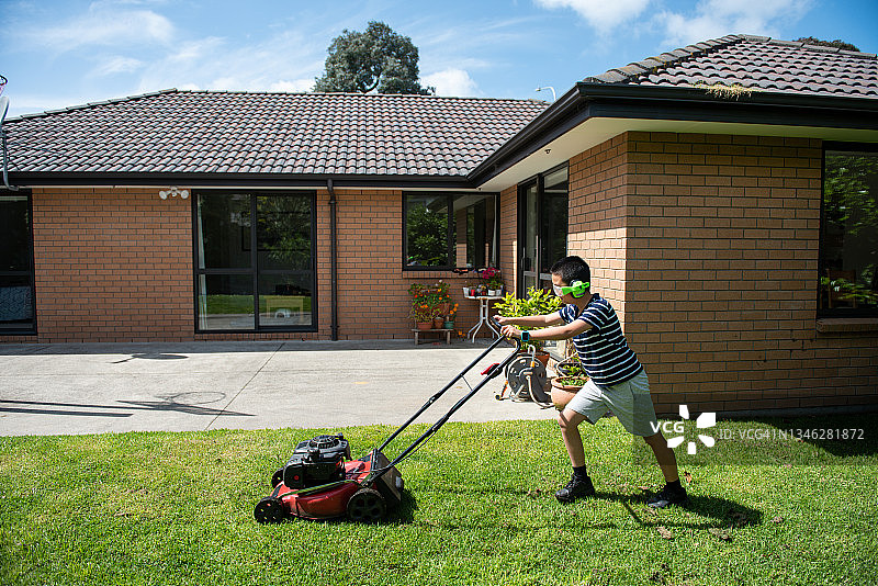 戴着耳机在后院割草的青少年男孩图片素材