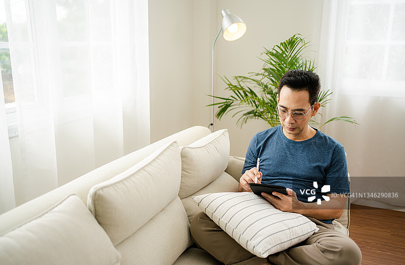 亚洲男人靠在沙发上用平板电脑放松图片素材