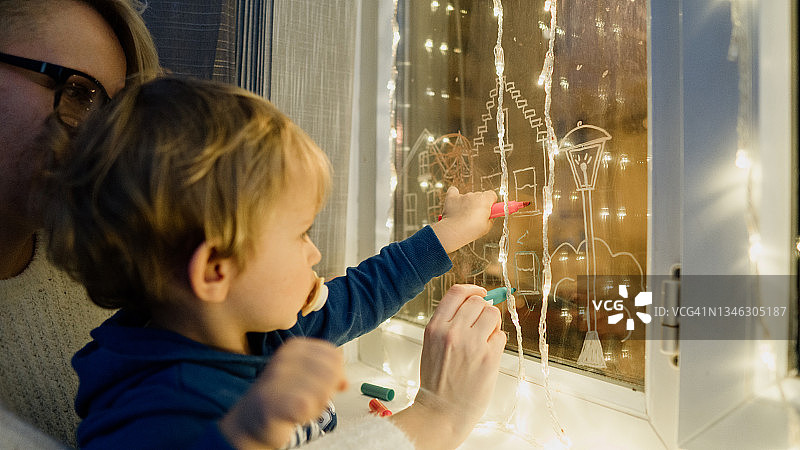 母子在窗户玻璃上绘制圣诞装饰画图片素材
