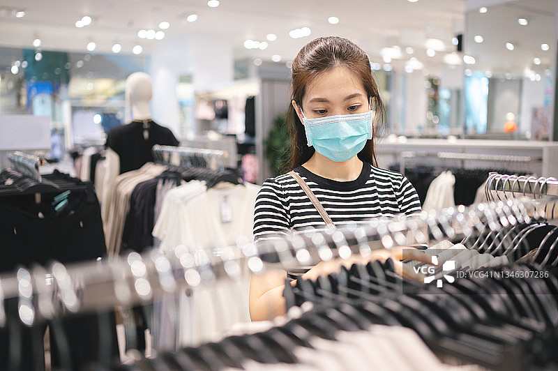 新常态下的快乐购物：戴防护口罩的年轻亚洲女性在下班后在城市服装店试穿衣服图片素材