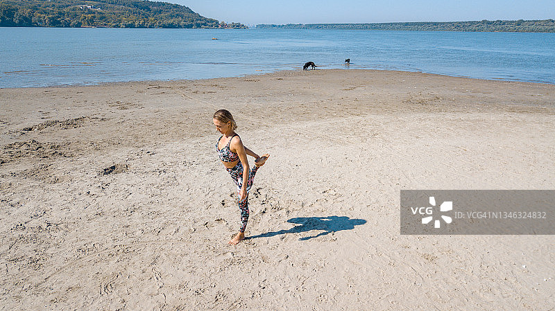 在沙滩上锻炼，伸展腿部的女人和她的影子的无人机航拍图片素材