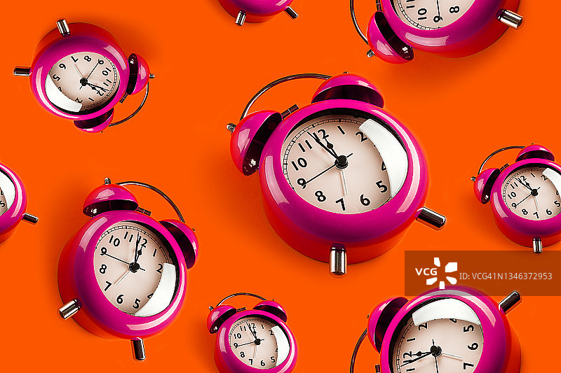红色或橙色背景上的一排粉色复古闹钟（时间流逝和生命流动的概念，无缝图案）图片素材