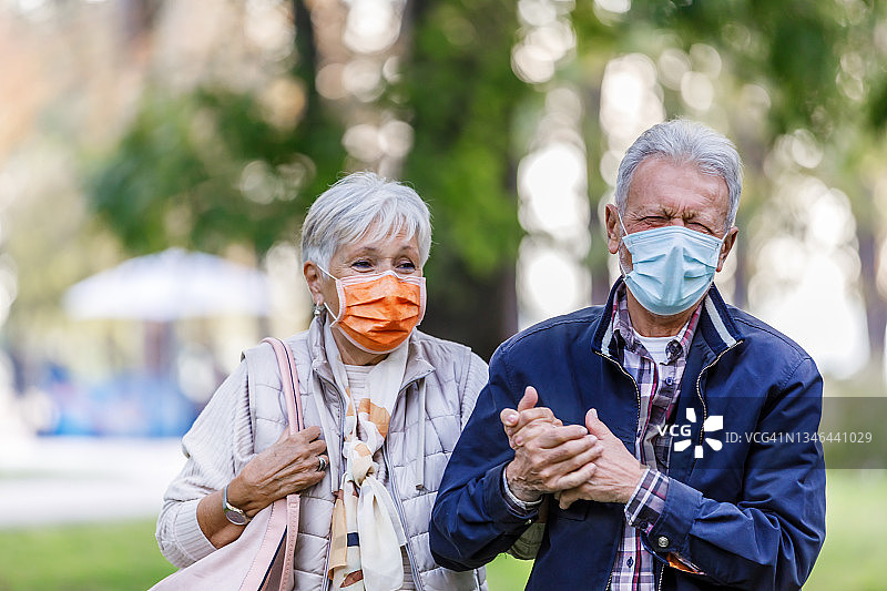 一对戴着口罩的快乐老年夫妇在公园里散步聊天图片素材