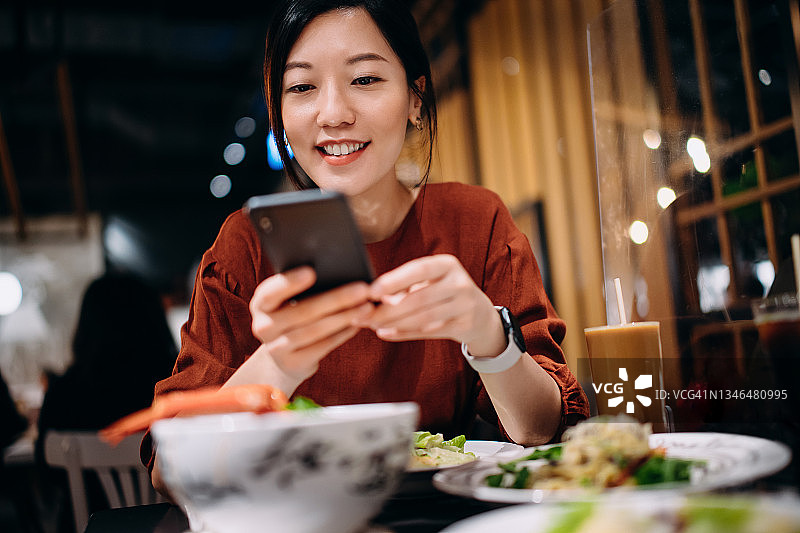 在泰国餐厅用手机拍摄美食的亚洲微笑女人图片素材
