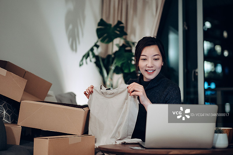年轻亚洲女性在家打开网购的纸箱，取出新买的衣服，对网购的可靠配送服务感到满意图片素材