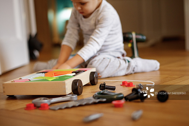 幼儿坐在拼花地板上玩木制玩具积木和手推车图片素材