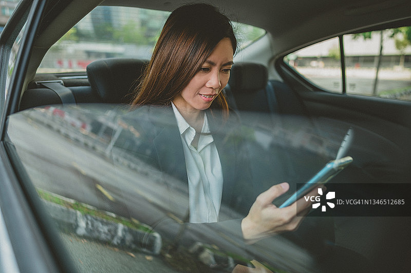 在汽车后座用智能手机发短信的亚洲女商人图片素材