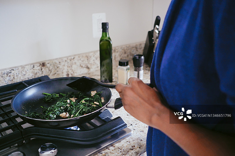 女人在炉子上炒菠菜和蘑菇图片素材
