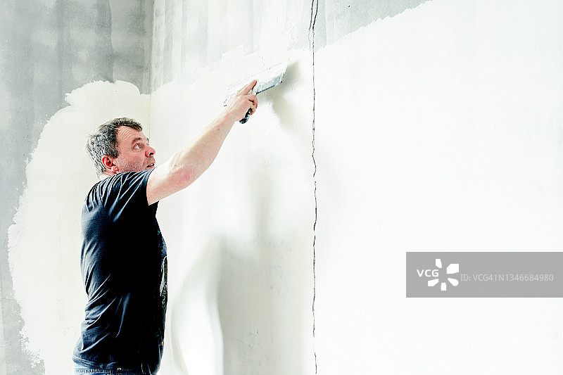 男油漆工在墙上涂腻子，墙上有裂缝图片素材