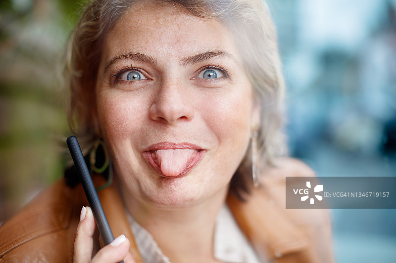 女人对着镜头吐舌头（使用手机）图片素材