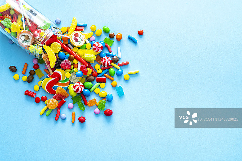 蓝色背景上洒出糖果的玻璃罐图片素材