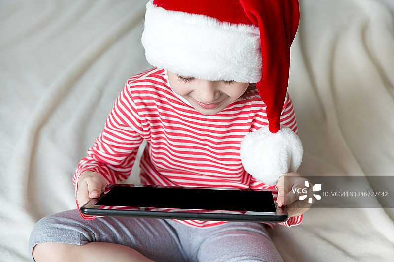戴红色圣诞帽玩平板电脑的儿童图片素材