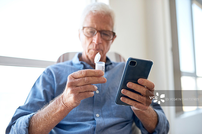 一位英俊的老年男人在养老院房间里发短信，手里拿着一盒药的局部照图片素材