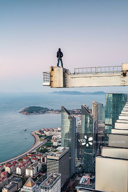 站在现代建筑屋顶窗户清洁器悬臂上的男人图片素材
