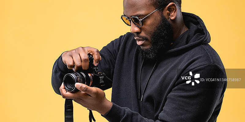 在工作室的专业摄影师，戴着黑色连帽衫和太阳镜的非裔美国男人正在使用数码相机工作图片素材