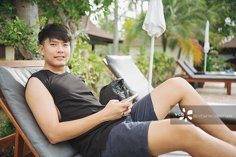 5G投资改变世界：亚洲女性在热带度假村度假时，通过手机阅读社交媒体和投资新闻，心情愉快图片素材