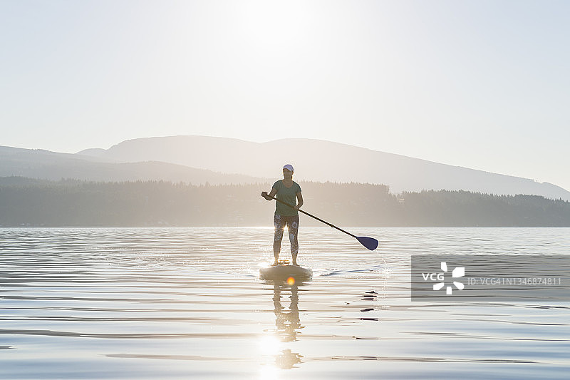 日出时分，女子在开阔水域划桨板图片素材