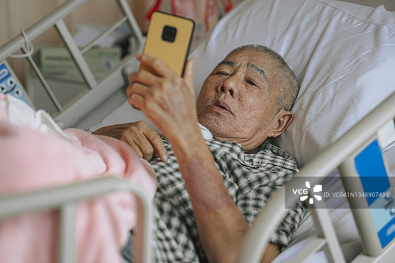 中国老人病人在医院病房床上用智能手机与家人视频通话图片素材