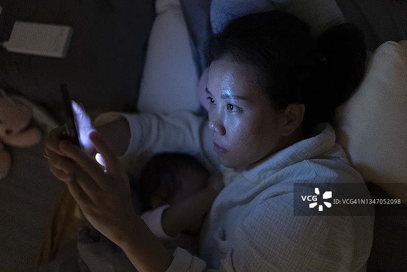 深夜在床上用手机，情绪积极的亚洲单身母亲给女儿喂奶图片素材
