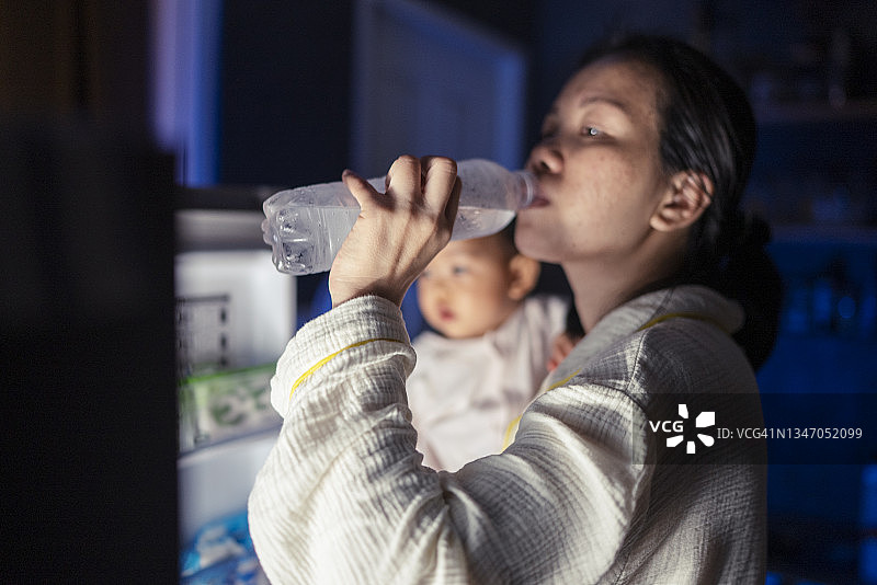 冰箱角度视图：亚洲年轻成人拥抱口渴的女儿，打开冰箱并在深夜喝清凉的淡水图片素材