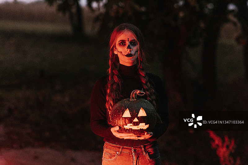一位化着舞台妆的年轻女子拿着万圣节雕刻的南瓜图片素材