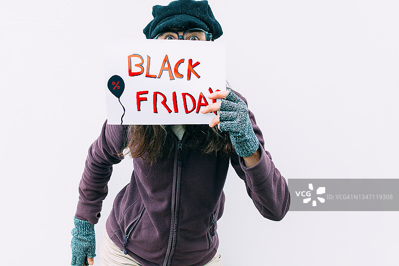 戴帽子和眼镜，面露惊讶表情，手持黑色星期五海报的女人图片素材