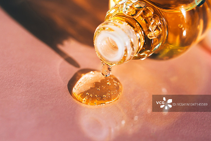明亮的黄色精油滴从玻璃瓶滴落，在粉红色背景上产生气泡图片素材
