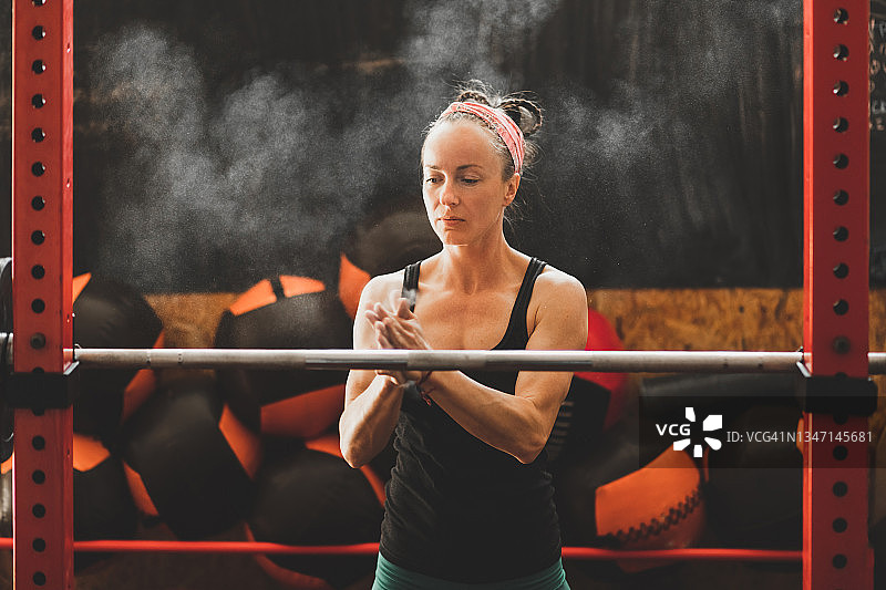 专注的女性使用运动镁粉，准备举起杠铃图片素材