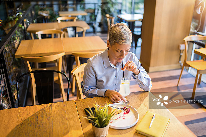 优雅的中年妇女在咖啡店喝柠檬水、吃美味的蛋糕图片素材