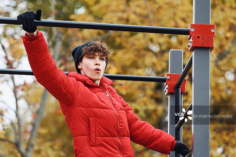 年轻女子在公共公园的单杠上做引体向上图片素材