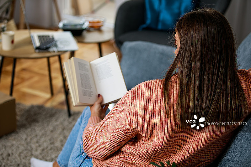 年轻女子躺在沙发上读书图片素材