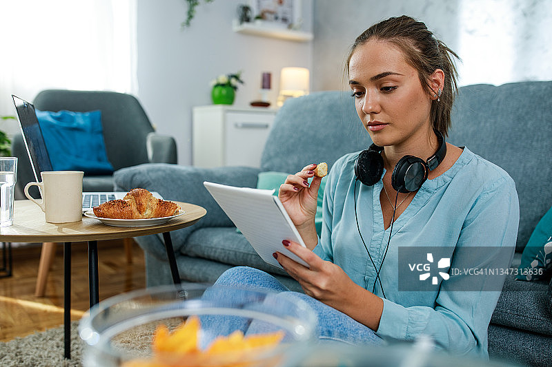 年轻女人在阅读笔记和学习时吃牛角面包图片素材